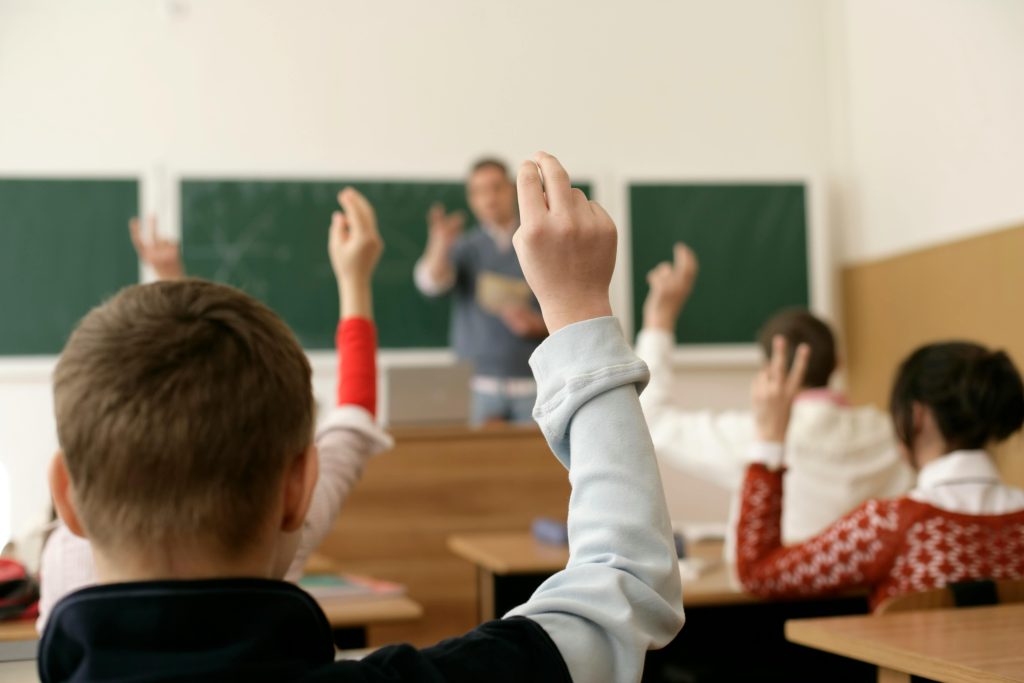 pexels photo 12716111 12716111 Students in a classroom raising hands, engaging in a lesson with the teacher.
